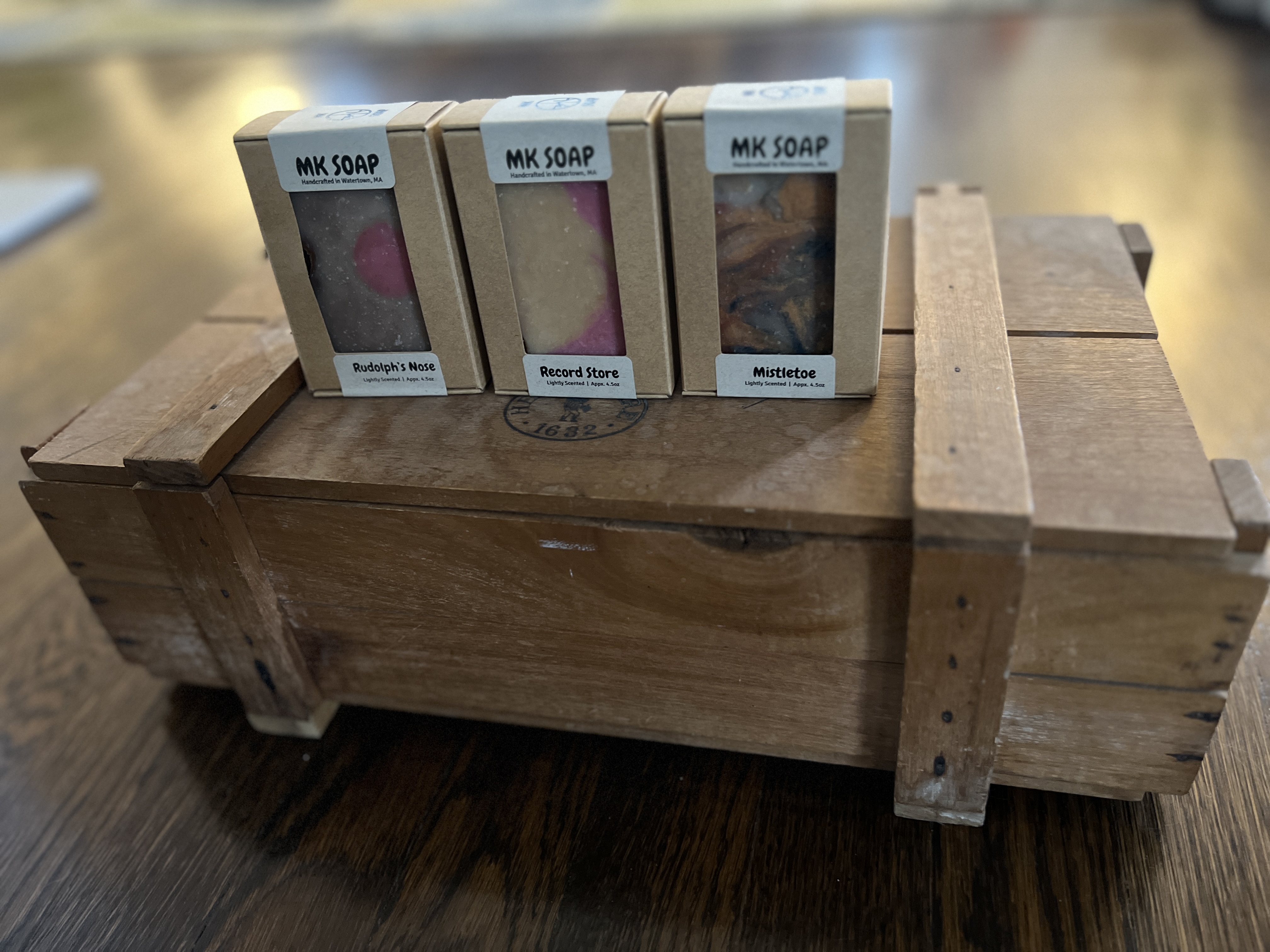 Three boxed MK Soap bars, Rudolph's Nose, Record Store and Mistletoe, on an antique wooden crate